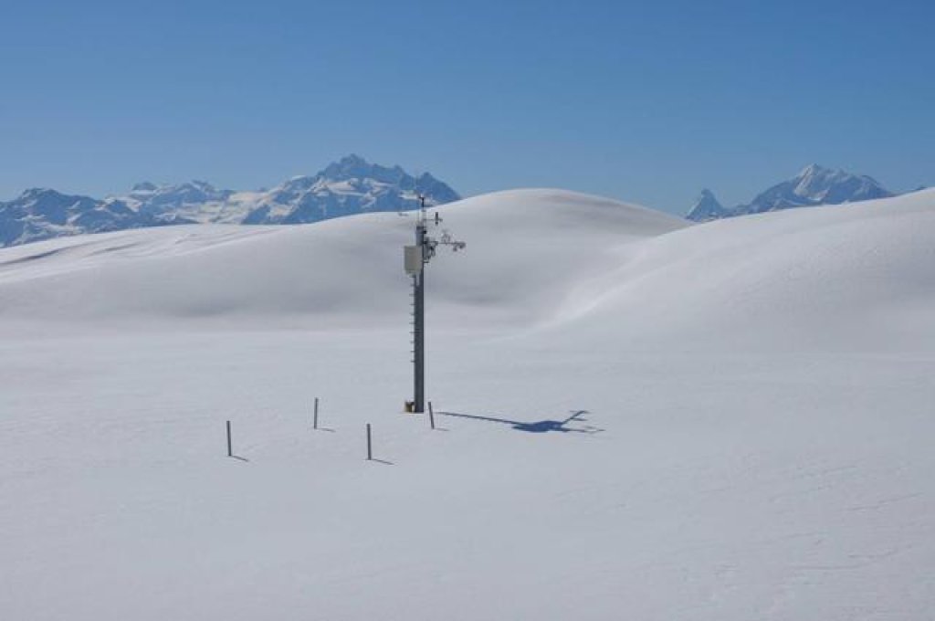 Schneestation Belalp: Die 4 sichtbaren Pfähle vor der Station  umzäunen im Sommer die Temperaturfühler und schützen diese so vor Wild- und Nutztieren.
